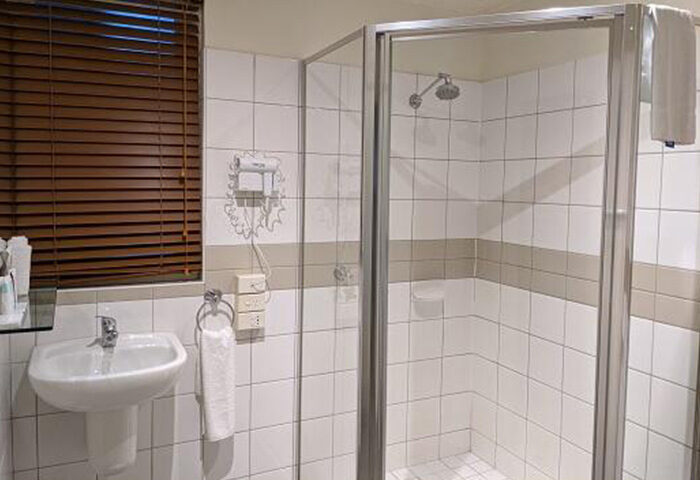 Bathroom at Tolarno Hotel, a cheap gay hotel in Melbourne's gayborhood, St Kilda. Sink, shower, and brown blinds visible.