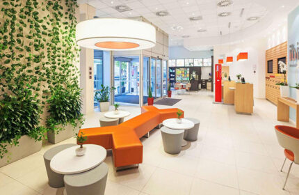 Ibis Praha Wenceslas Square Hotel lobby. Modern design with plants, orange seating, and reception. Gay-friendly hotel near Prague nightlife.