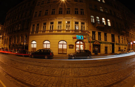 EA Hotel Tosca in Prague at night. Cheap gay hotels near gay nightlife. Cars on cobblestone street, fisheye view.