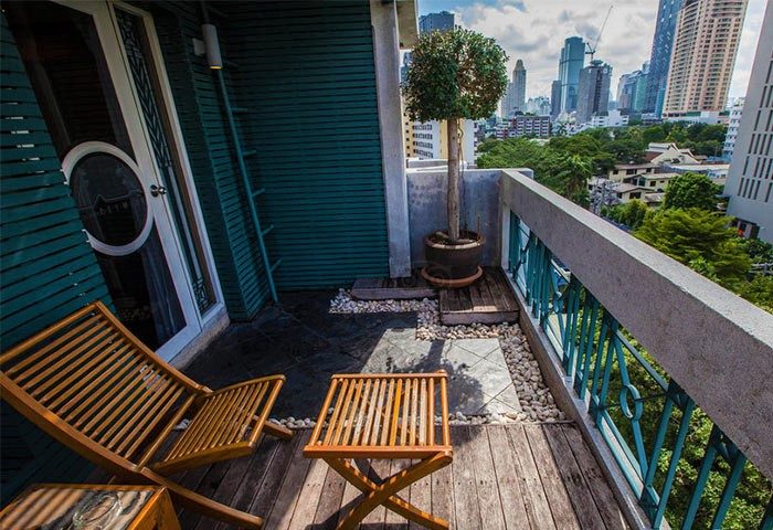 Babylon Bangkok Hotel balcony view. Gay men's hotel with sauna, affordable stay. Bangkok skyline, wooden chairs, and tropical plants.