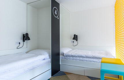 Meetme23 Hotel: Cheap gay party hostel in Prague's gayborhood. Interior view of a room with two beds, reading lamps, and a stool.