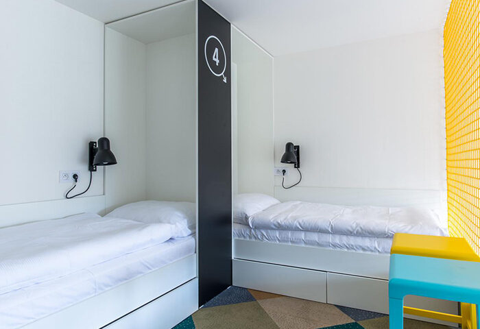 Meetme23 Hotel: Cheap gay party hostel in Prague's gayborhood. Interior view of a room with two beds, reading lamps, and a stool.
