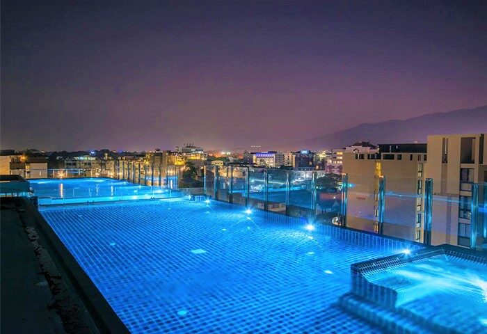 Night view of a luxury hotel rooftop pool in Nimman, Chiang Mai. LGBT-friendly stay with city skyline.