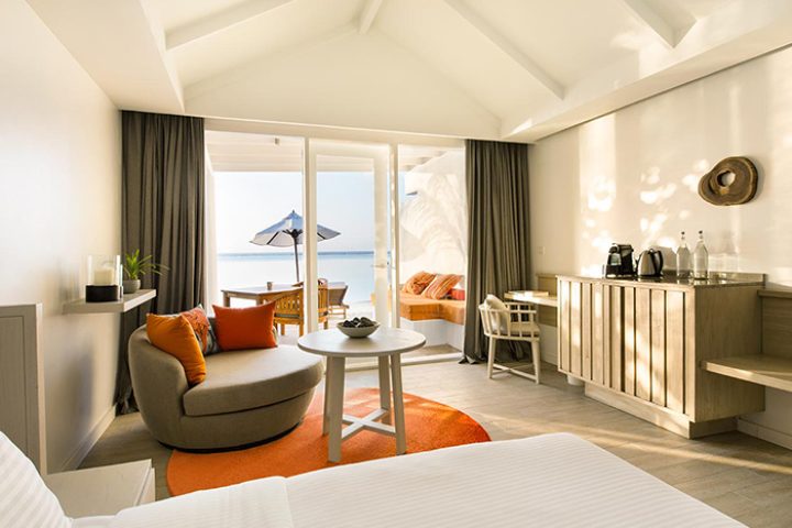LUX* South Ari Atoll Maldives villa interior. Beach view from luxury gay honeymoon hotel. Round sofa, table, and desk in a bright, modern room.