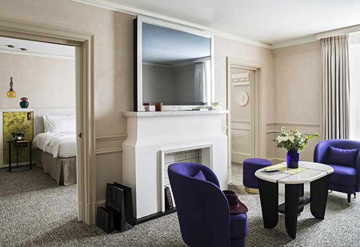 Sofitel Le Scribe Paris Opéra hotel room. Luxury Paris hotel in Marais gayborhood. Purple chairs, fireplace, bedroom view. Gay honeymoon.