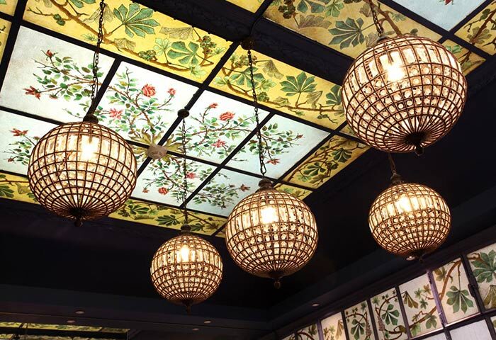 Ceiling detail at Little Palace Hotel, a cheap luxury gay hotel in Paris' Marais gayborhood. Globe lights hang from a floral stained glass ceiling.