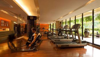 Hilton Phuket Arcadia Resort & Spa gym. Man using leg press, woman on treadmill. Luxury gay hotel with pool and gym in Thailand.