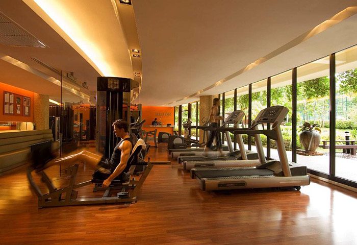 Hilton Phuket Arcadia Resort & Spa gym. Man using leg press, woman on treadmill. Luxury gay hotel with pool and gym in Thailand.