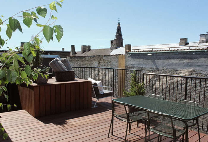 Hotel Herman K by Brøchner Hotels rooftop garden in Nyhavn. Luxury gay hotel with a table and chairs, plants, and a view of the city.