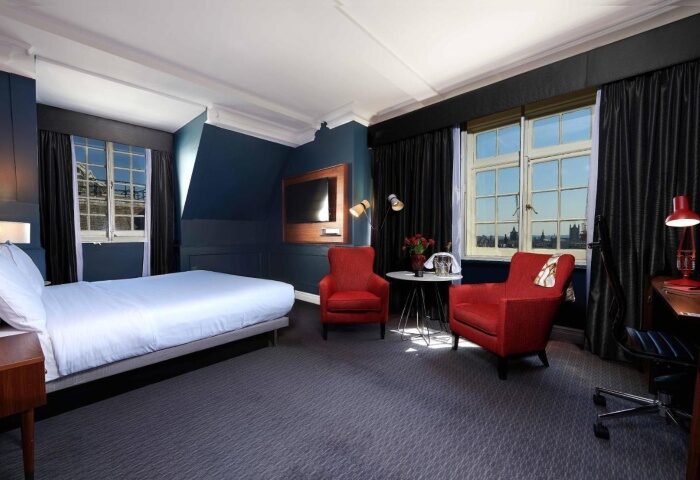 The Dilly hotel room. Cheap luxury gay hotel in London. Room with bed, red chairs, desk, and city view. Gay travel advice.