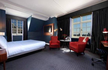 The Dilly hotel room. Cheap luxury gay hotel in London. Room with bed, red chairs, desk, and city view. Gay travel advice.