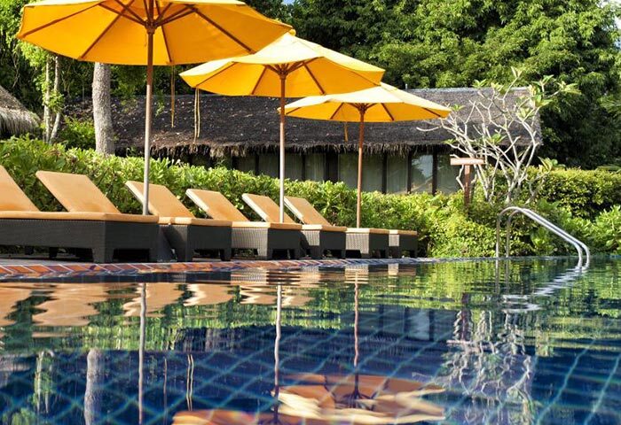 Zeavola Hotel beachfront pool view. Gay-popular, cheap luxury hotel in Phi Phi. Sun loungers and yellow umbrellas reflect in the pool's blue water.
