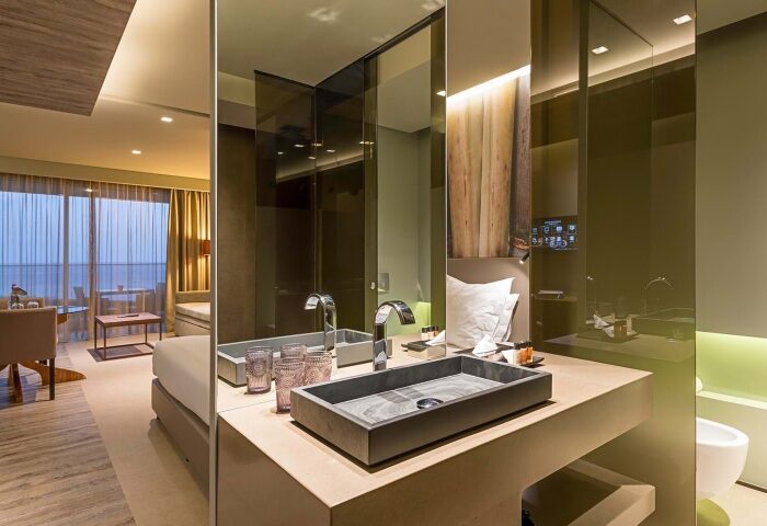 Saccharum Hotel, Madeira, Portugal. Luxury spa hotel bathroom. Modern design with stone sink, mirror, and partial view of the room. Gay travel.