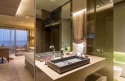 Saccharum Hotel, Madeira, Portugal. Luxury spa hotel bathroom. Modern design with stone sink, mirror, and partial view of the room. Gay travel.