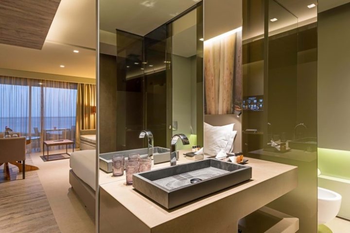 Saccharum Hotel, Madeira, Portugal. Luxury spa hotel bathroom. Modern design with stone sink, mirror, and partial view of the room. Gay travel.