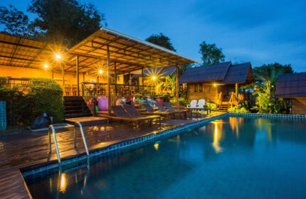 Phi Phi's Cobble Beach Hotel rooftop pool at dusk. Gay travel lodging with beachfront access. Deck chairs, cabanas, and wooden bungalows.