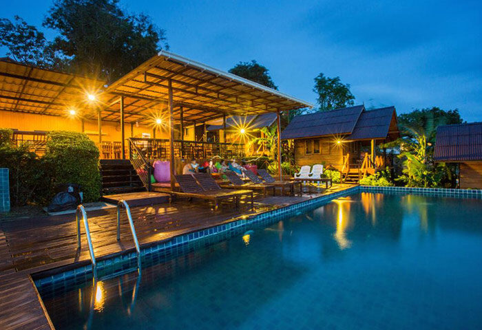 Phi Phi's Cobble Beach Hotel rooftop pool at dusk. Gay travel lodging with beachfront access. Deck chairs, cabanas, and wooden bungalows.