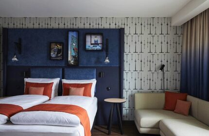 Hotel Indigo Berlin East Side Gallery room. Twin beds, blue headboard, art, and sofa. Popular gay hotel in Berlin. Cheap hotel deal.