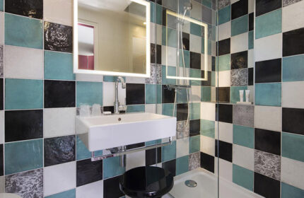 Les Tournelles Hotel, Paris bathroom. Chic design with black, white & teal tiles. Modern sink, lighted mirror & stool. Gay travel.