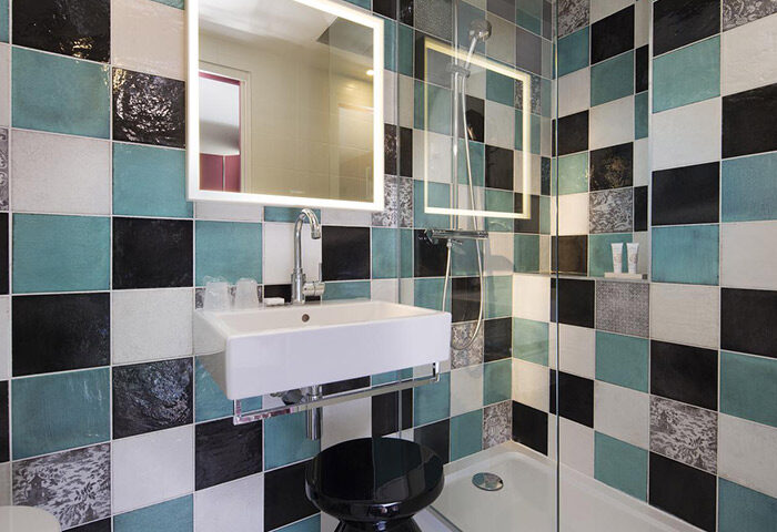 Les Tournelles Hotel, Paris bathroom. Chic design with black, white & teal tiles. Modern sink, lighted mirror & stool. Gay travel.