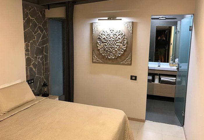 Villa Adler Gay Men Only room. Bedroom with bed, stone wall, and bathroom view. Gay hotel in Playa del Ingles near Yumbo Center.