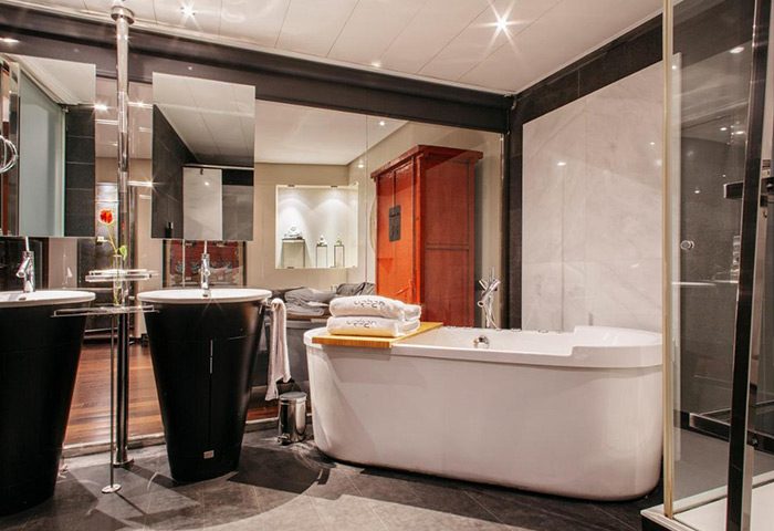Urban Hotel Madrid bathroom. Luxury gay hotel with modern design, featuring a bathtub, black vessel sinks, and a mirrored wall. City center stay.