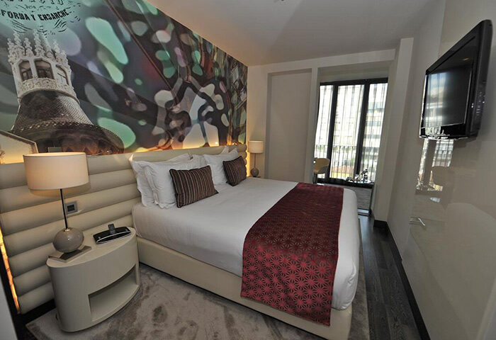 Hotel Indigo Barcelona Plaza Catalunya room. Upscale gay hotel with double bed, modern art, and TV. Cheap price for luxury stay.
