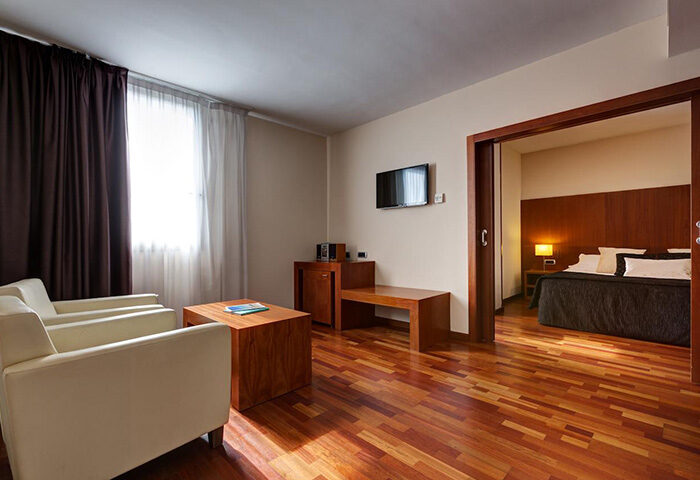 Acevi Villarroel Hotel room. Upscale Barcelona hotel near gay bar. Modern interior, wood floors, two chairs, TV, and a view into the bedroom.