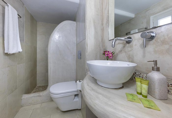 Carbonaki Hotel's upscale bathroom in Mykonos. Modern design with a white sink, toilet, and shower. A cheap, gay-friendly hotel option.