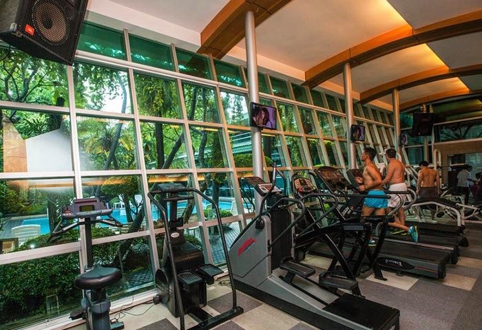 Babylon Bangkok Hotel gym. Gay men work out on treadmills overlooking the pool. Modern fitness center at a men-only hotel.