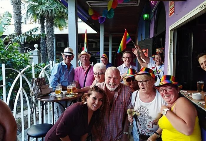 Chessa Bar, a gay bar in Torremolinos. Group of happy people with rainbow hats and flags, enjoying drinks at this popular gay venue.