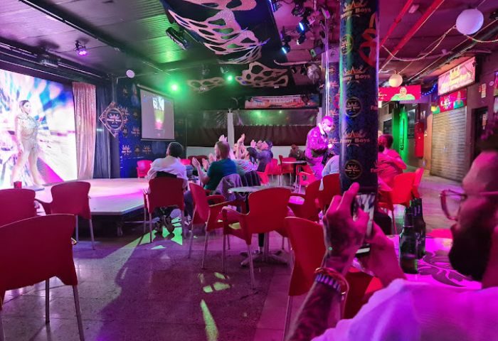 Chez Funny Boys gay bar in Gran Canaria. Drag show performance on stage, audience clapping. Gay travel destination, nightlife scene.