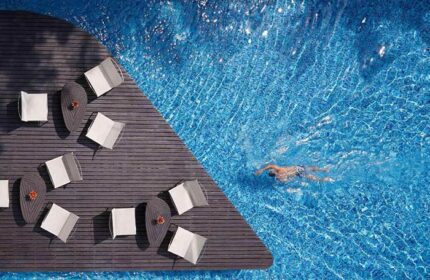 Baraquda Pattaya Mgallery: Chic design gay hotel in Pattaya with pool. Man swims in clear blue water near lounge chairs on a wooden deck.