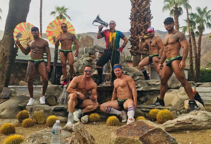 Chill Bar Performers: Group of muscular gay men at a Palm Springs event. Some are shirtless, wearing swim briefs, and posing near a waterfall.