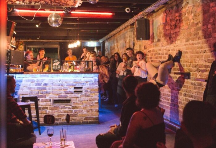 Ching-a-Lings Sydney: Gay bar with drag performance on a brick wall. Crowd watches, bar with drinks, disco ball. Gay travel advice.