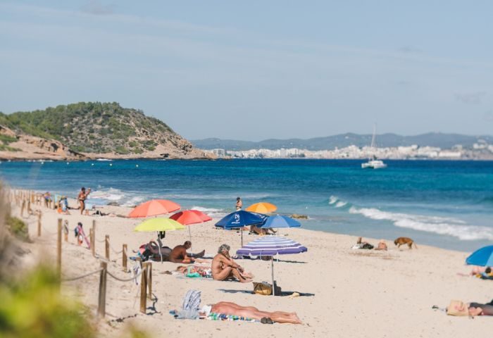 Chiringay Gya Bar and Beach in Ibiza. Sandy beach with people sunbathing under colorful umbrellas. Gay travel destination.