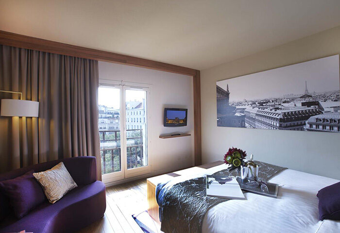 Citadines Les Halles Paris room. Modern gay-friendly hotel in Marais gayborhood. Comfy bed, purple couch, Paris view. Most booked hotel.