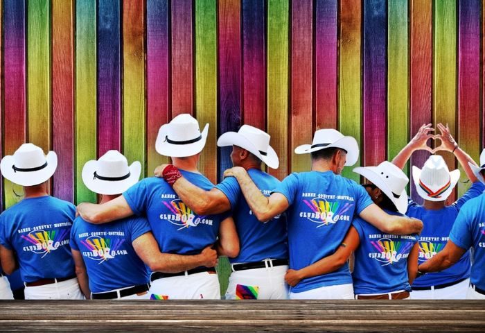 Montreal gay dance party at Club Bolo. Men in cowboy hats and matching shirts pose against a colorful wooden wall. Gay travel.