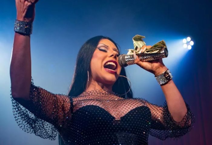 Drag queen performing at Club Cobra, a gay bar. She's holding a microphone with cash, wearing a sparkly dress & bracelets.