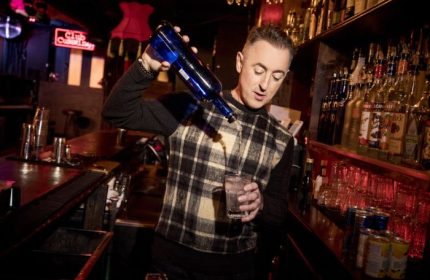 Alan Cumming pours a drink at his gay bar Club Cumming in New York. Gay travel advice.