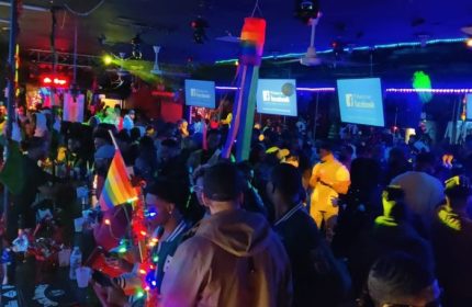 Crowded Chicago gay club party. Rainbow flags, colorful lights, and Facebook signs. Escape Drag Shows event. Gay men travel.