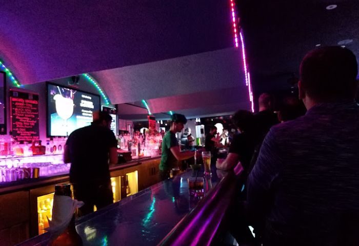 Inside Club OMG, a gay bar in San Francisco. Bartender serving drinks, patrons at the bar, purple lighting. Gay travel advice.