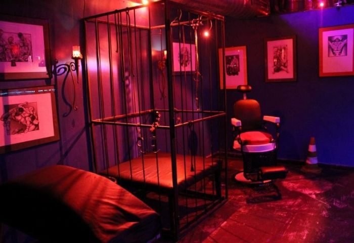 Club Open Mind, Barcelona. Gay cruise club interior with a cage, chair, and erotic art. Red lighting, suggestive atmosphere. Gay travel.