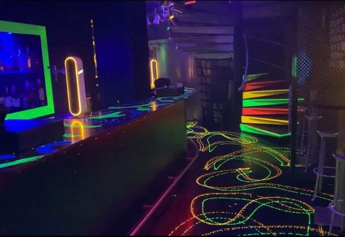 Inside Club XXL, a gay club in Sitges. Neon lights illuminate the bar and floor. Spiral staircase adds to the club's vibrant atmosphere.