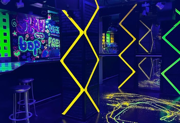 Interior of Club XXL, a gay club in Sitges, Spain. Neon lights, graffiti art on the walls, bar stools, and a vibrant, energetic atmosphere.