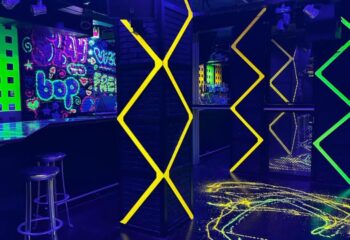 Interior of Club XXL, a gay club in Sitges, Spain. Neon lights, graffiti art on the walls, bar stools, and a vibrant, energetic atmosphere.