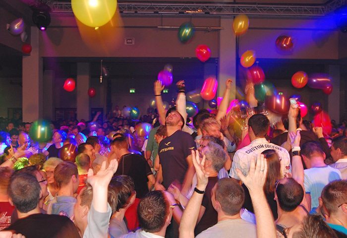 Club78 Frankfurt: A crowded gay club scene with men dancing under colorful balloons and vibrant lighting. Gay travel advice, nightlife.