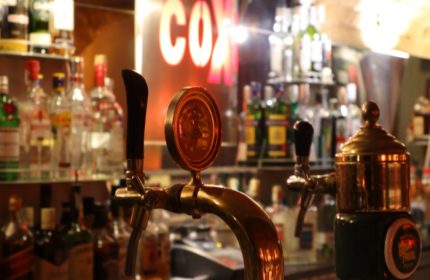 Coxx Men's Bar interior, Budapest. Beer taps and bottles on shelves. Gay travel advice. Nightlife scene, bar setting.