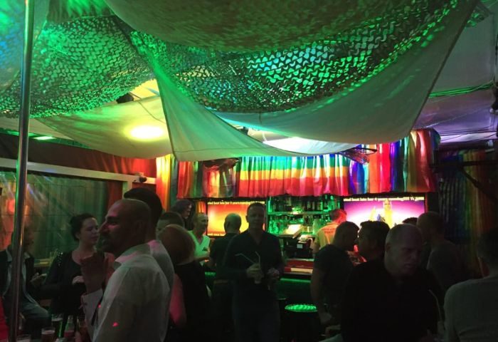 Interior of Coco Loco Gay Bar in Gran Canaria. Crowd of people, rainbow flag, camouflage netting, and green lighting.