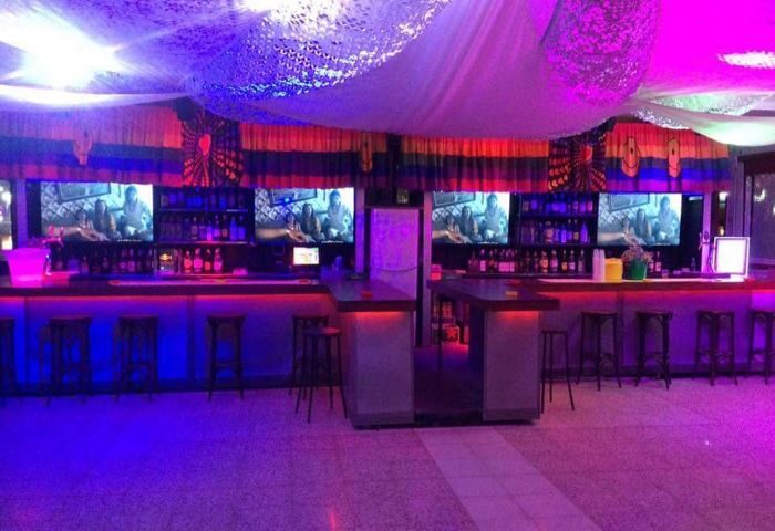 Coco Loco Gay Bar in Gran Canaria. Interior view, bar with stools, TV screens, bottles, purple and red lighting. Gay travel advice.